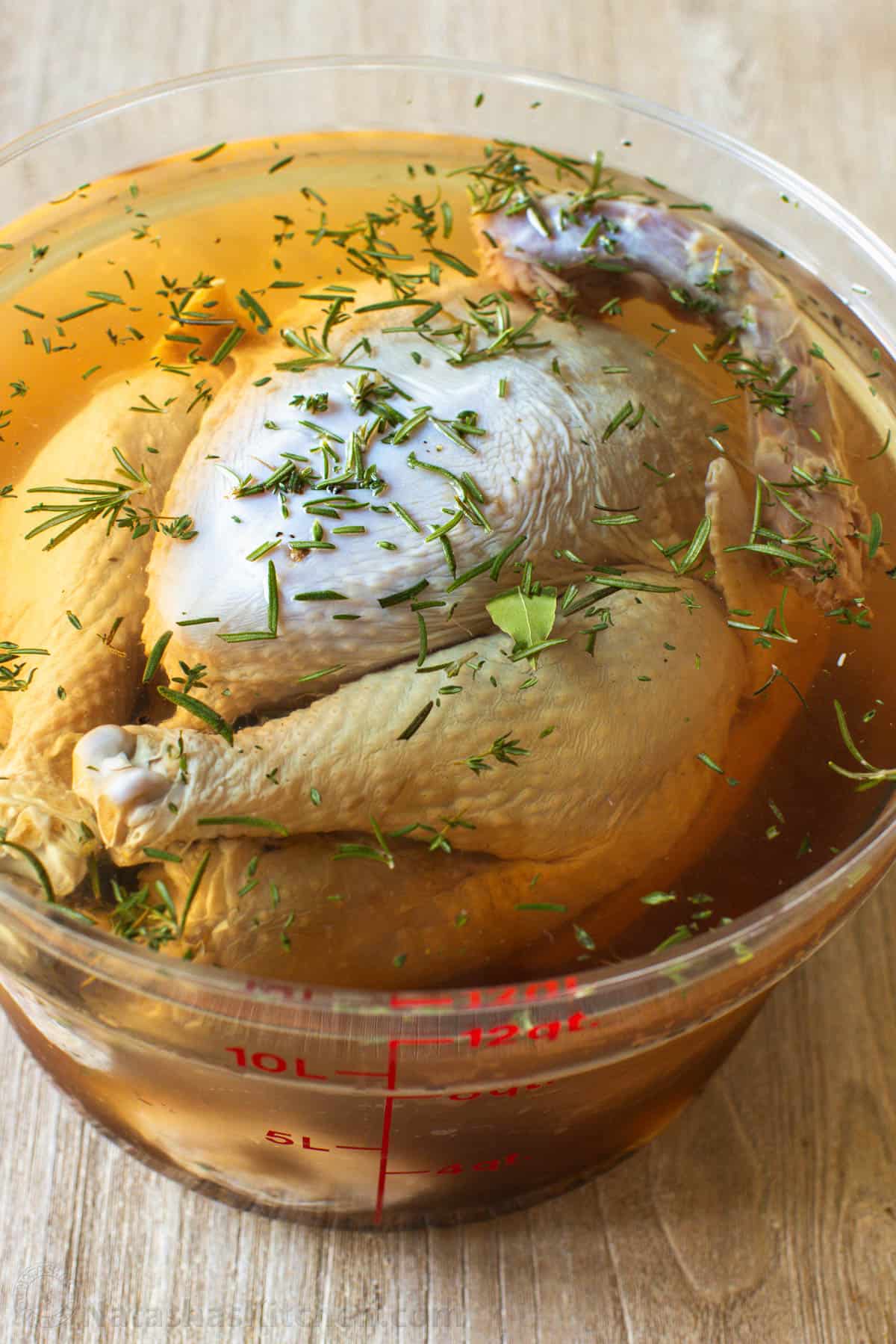 A whole turkey soaking brine with herbs sprinkled on top