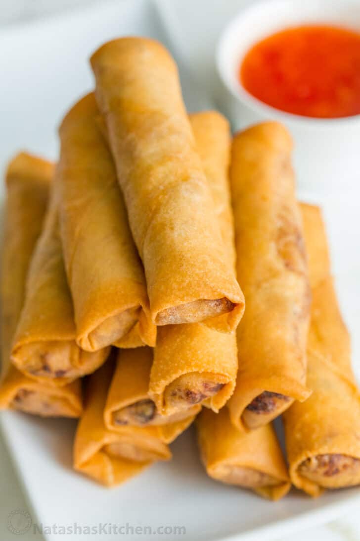 Egg rolls stacked on a plate with sauce in the background