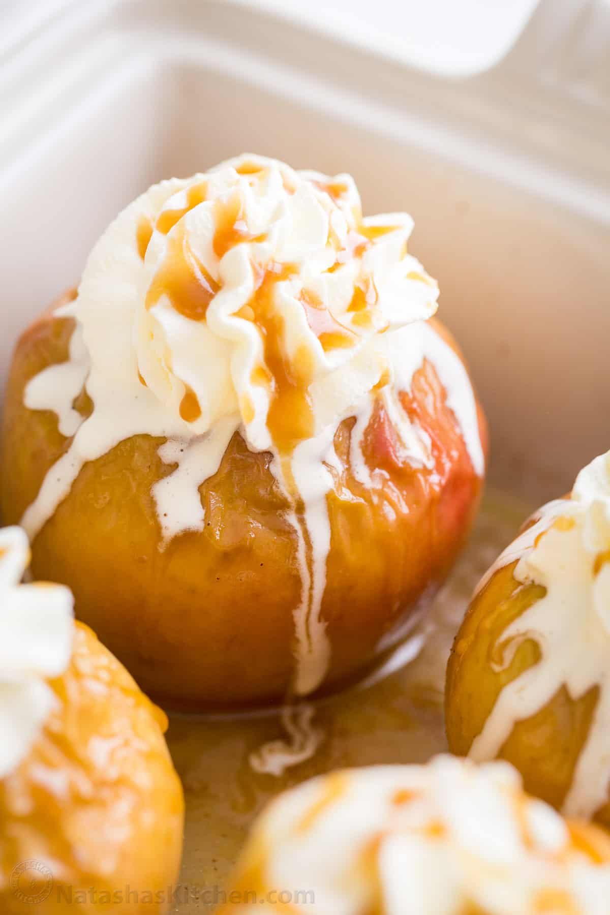 Baked apples in a baking dish topped with whipped cream and caramel sauce.
