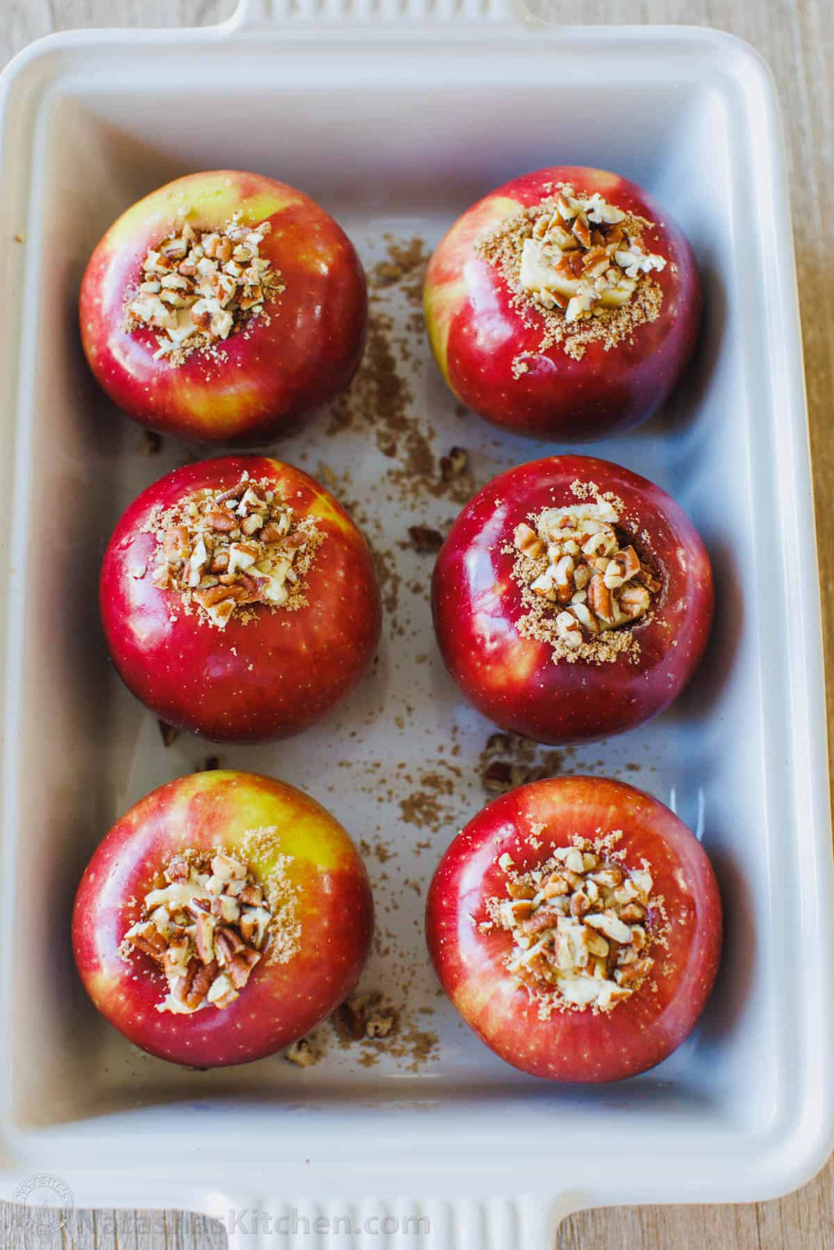 Unbaked apples stuffed with cinnamon sugar filling arranged in a baking dish.
