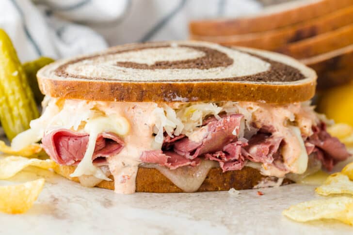 Classic Reuben on a plate with pickles and chips.