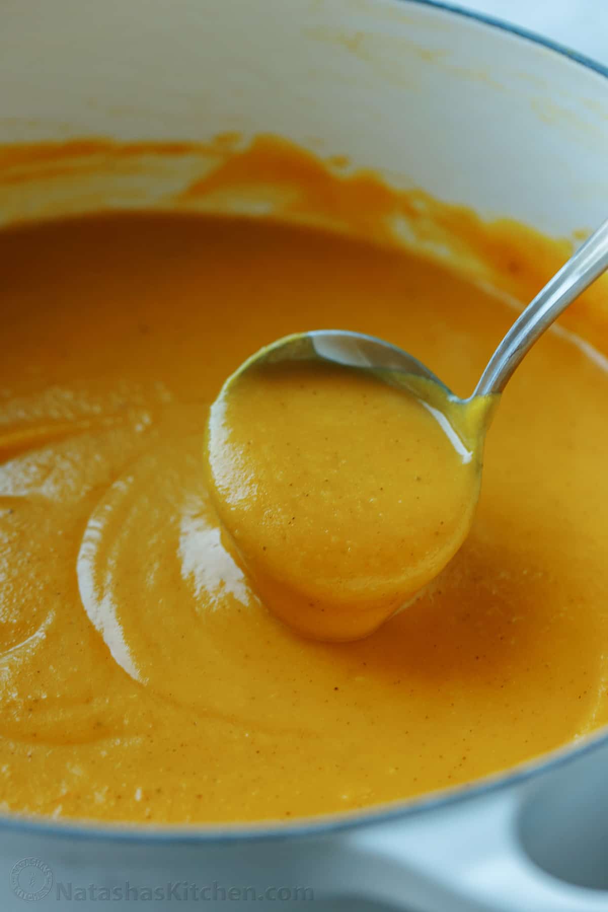 A ladle scoops butternut squash soup from a large pot.