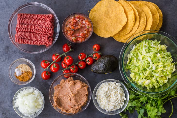 Tostada ingredients with tortillas, refried beans, ground beef, and lettuce