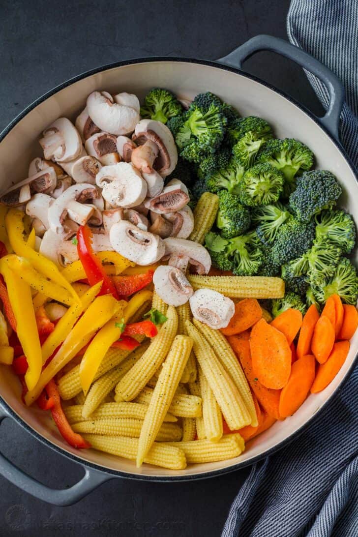 Vegetables cut and prepped in a skillet for stir fry recipe with a towel on the side of the skillet.
