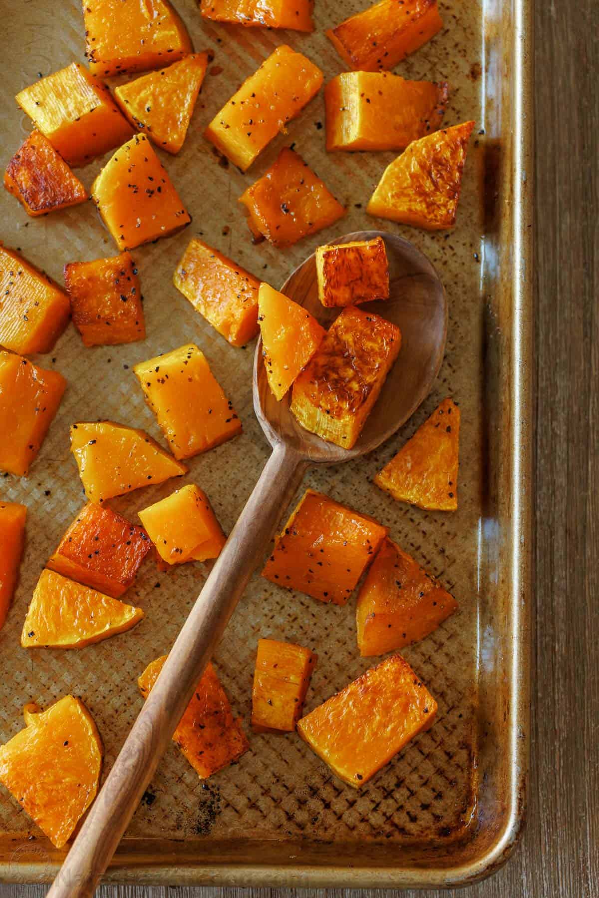 Close up of roasted butternut squash chunks on a metal baking sheet with a spoon.