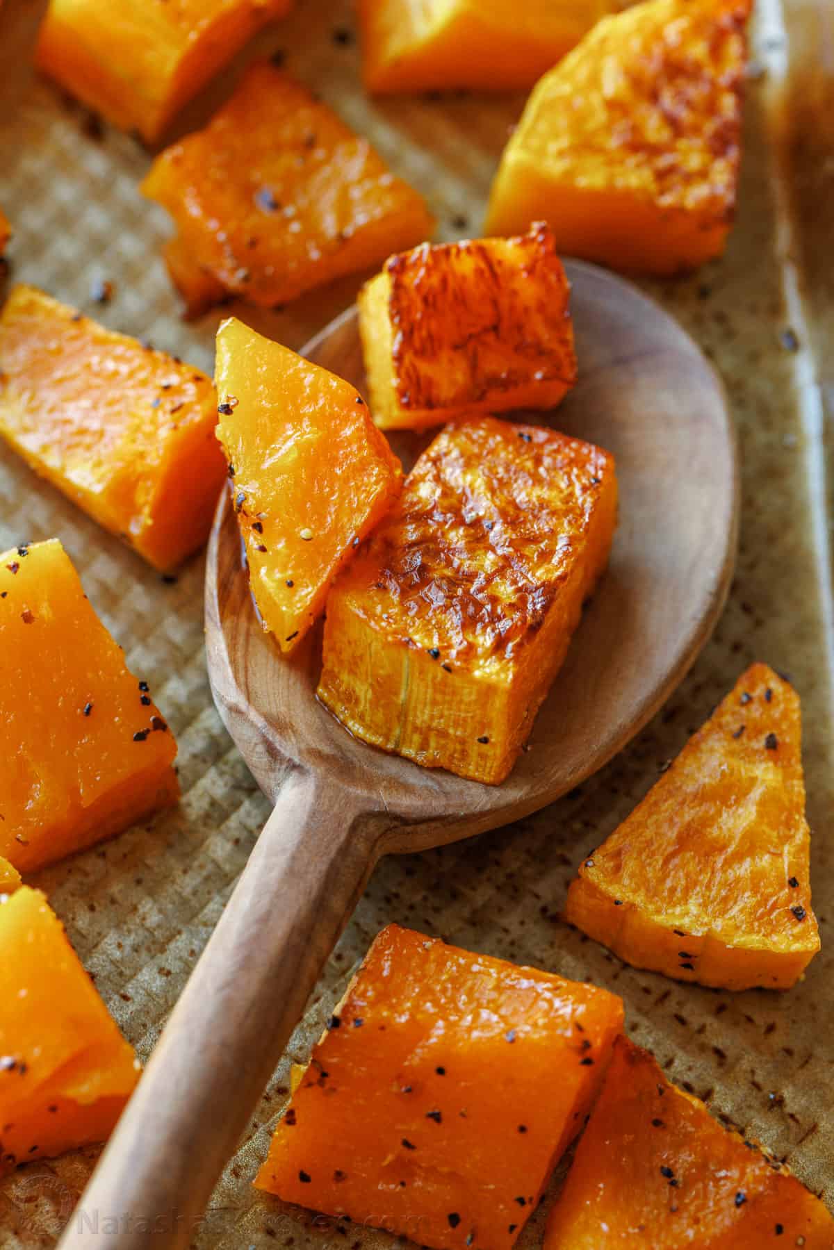 Close up of roasted butternut squash chunks on a metal baking sheet with a spoon.