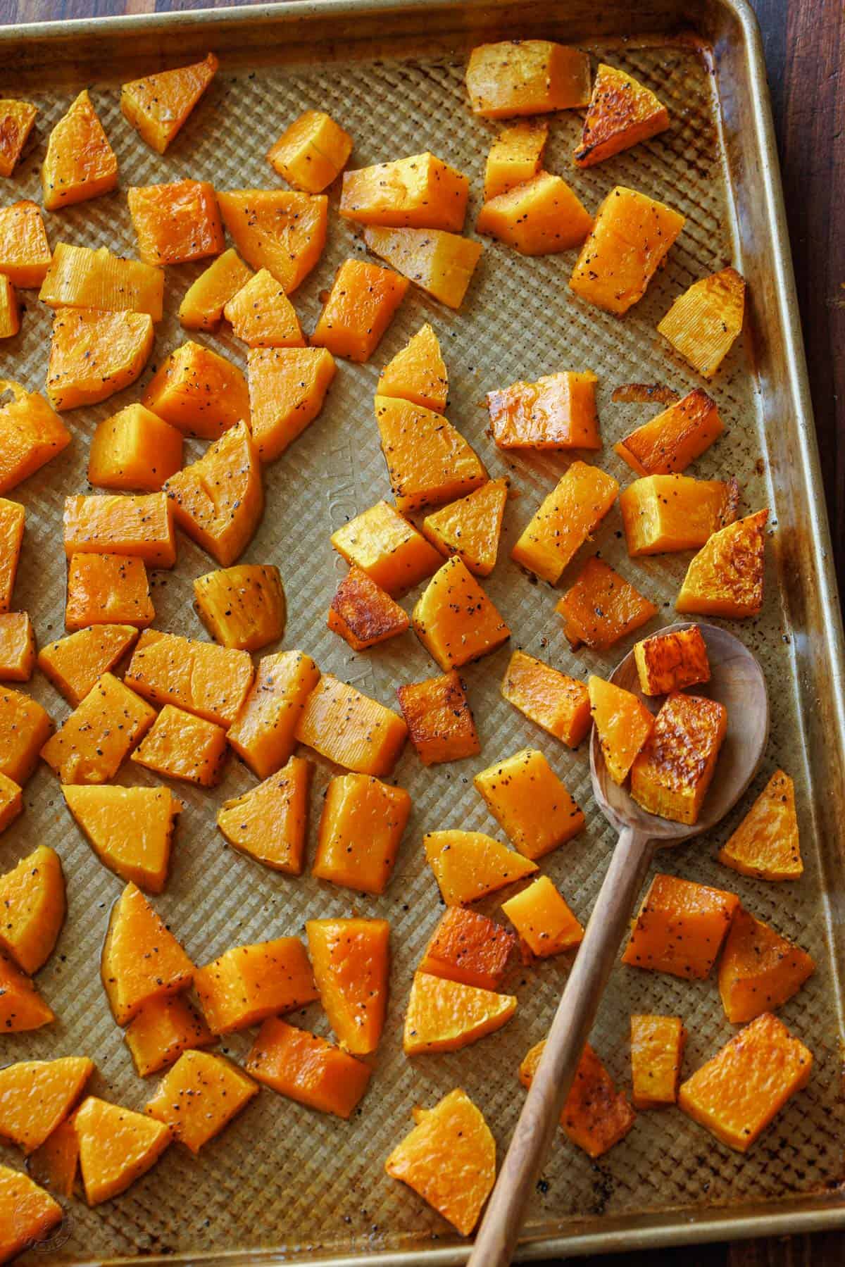 Roasted butternut squash roasted ahead on a metal baking sheet with a spoon.