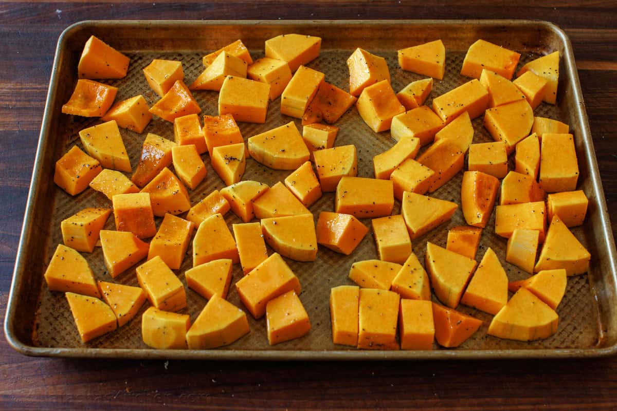 Morceaux de courge musquée coupés et assaisonnés sur une plaque de cuisson en métal.