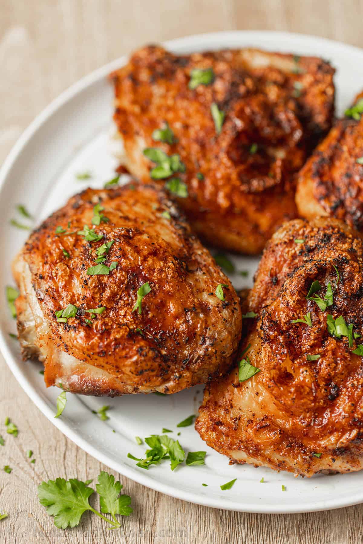 Quatre cuisses de poulet à la friteuse à air sur une assiette blanche garnie de persil frais haché.