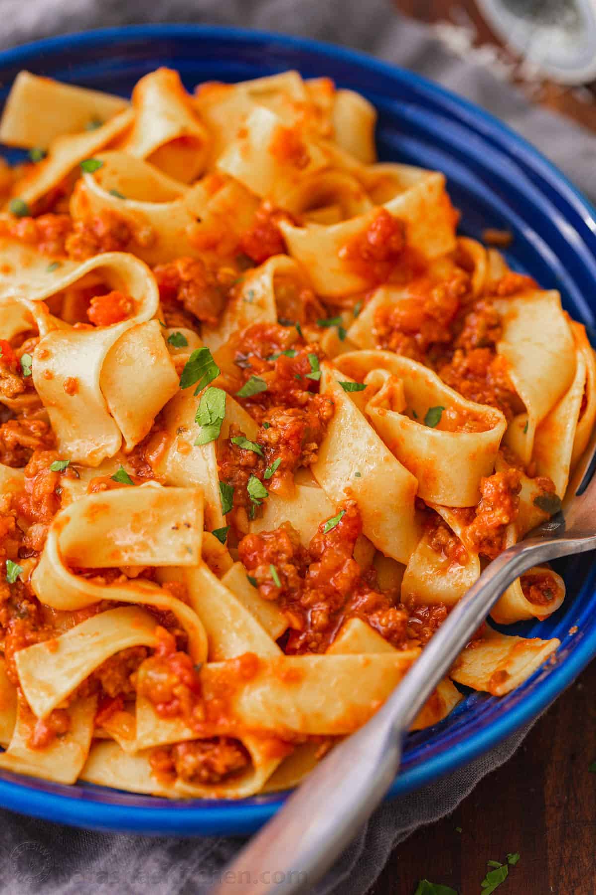 Pappardelle pasta with bolognese sauce in a blue bowl, with a fork.