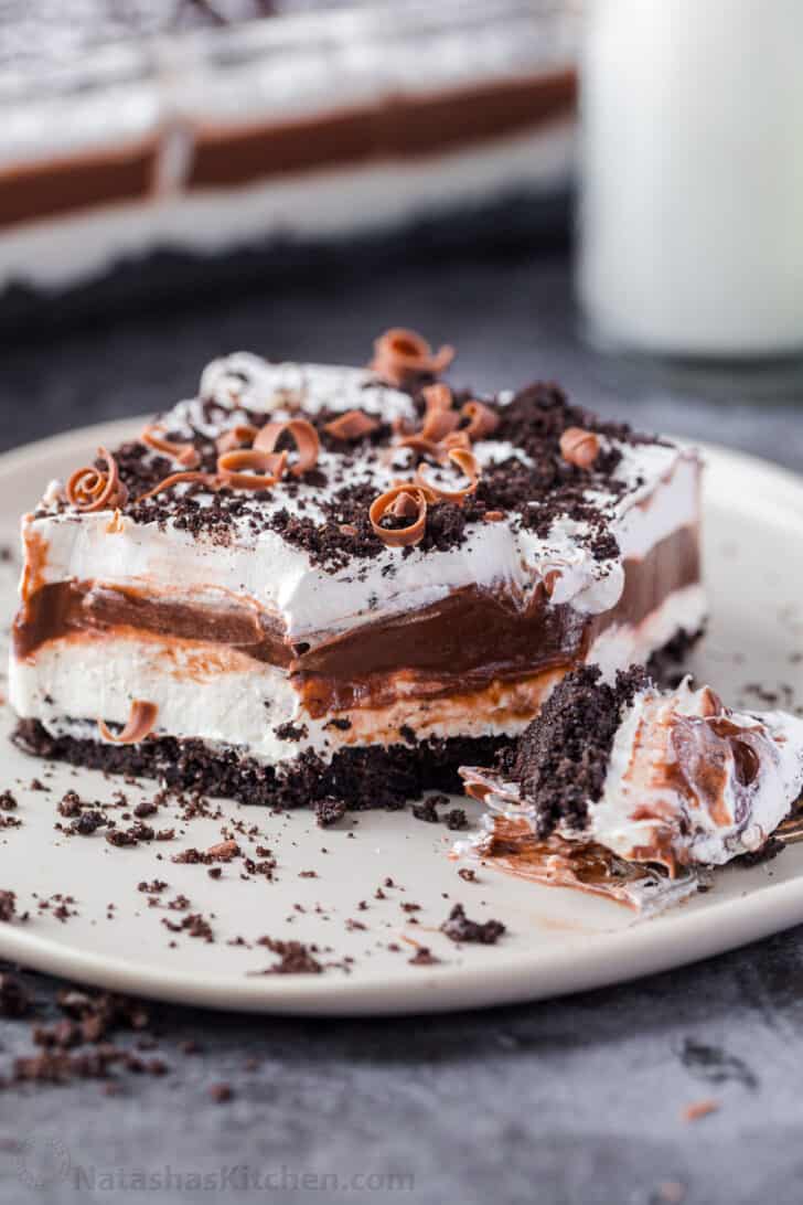 A slice of layered chocolate lasagna topped with crushed oreos and chocolate shavings on a white plate.