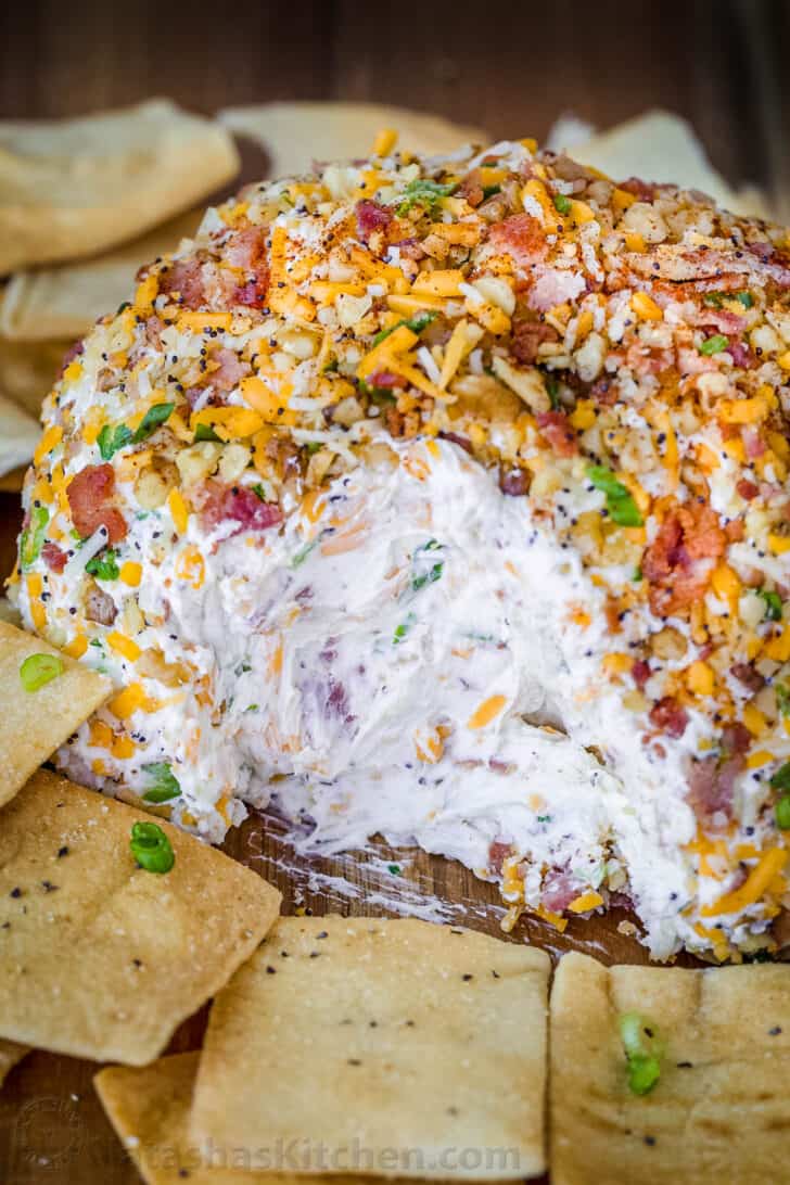 Cheese ball coated with bacon, cheese and nuts on a serving plate.