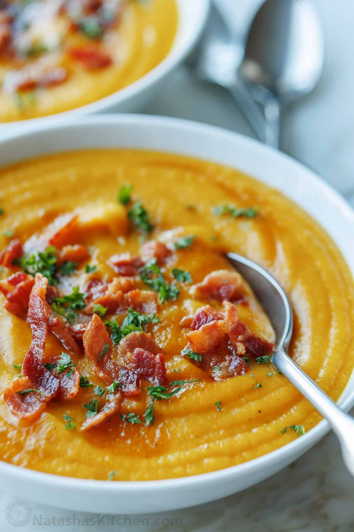 A bowl of homemade butternut squash soup garnished with bacon and parsley, with a spoon.