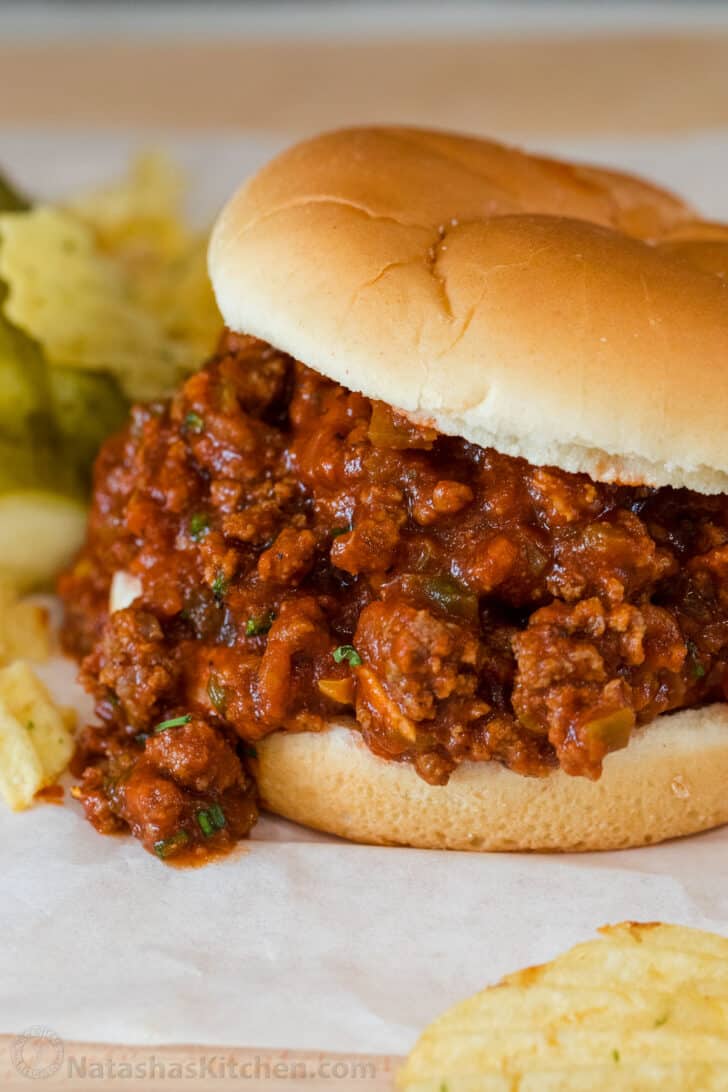 Sloppy joe sandwich on a plate with chips and pickles.