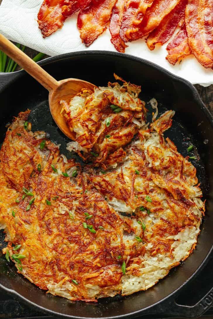 Crispy hash browns in a skillet served with bacon.